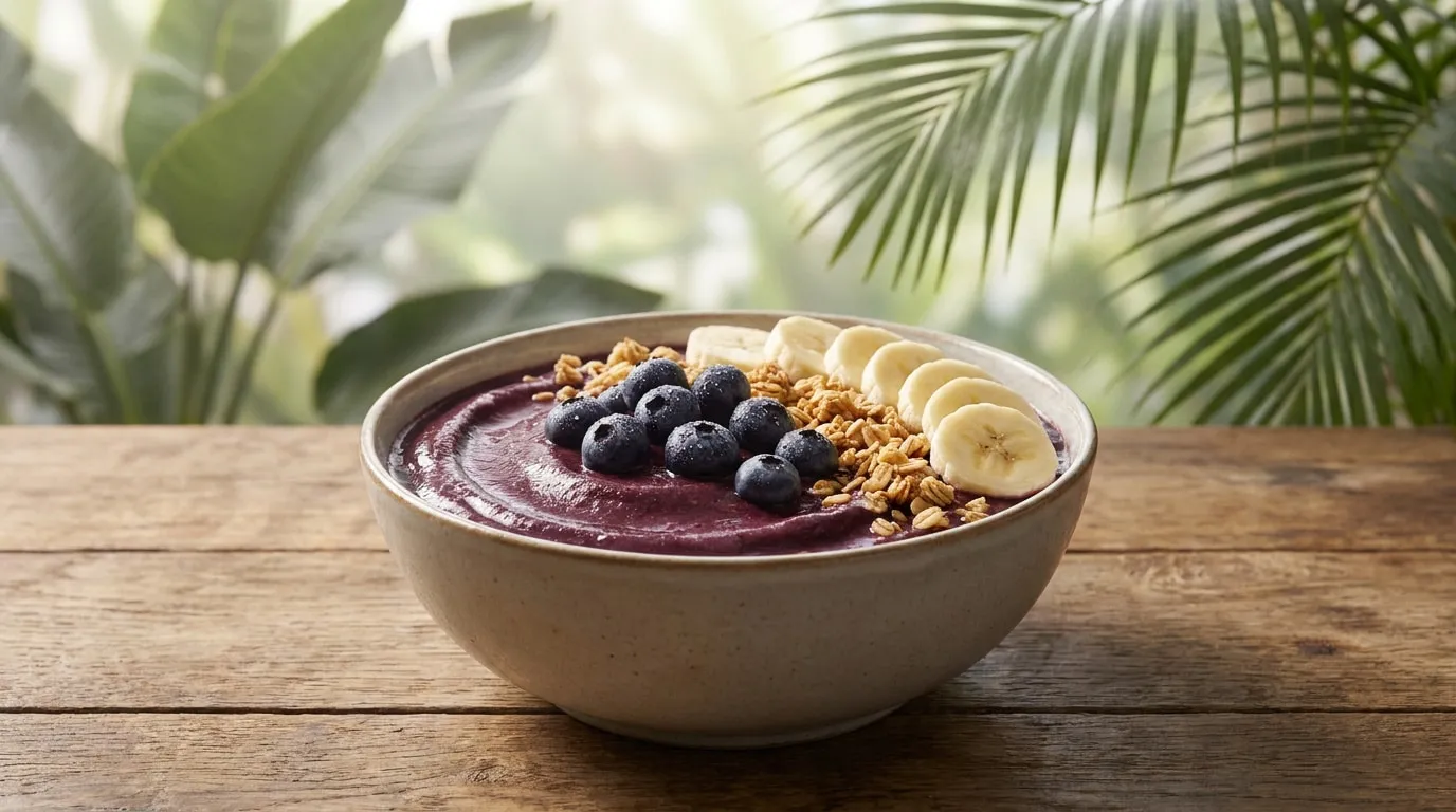 Un bol d'açaï violet garni de myrtilles, de rondelles de banane et de granola sur une table en bois avec des feuilles.