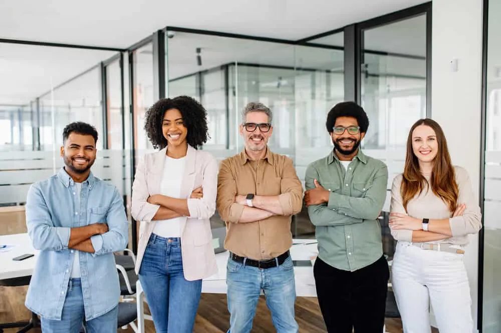 Cinq collègues souriants posent ensemble au bureau.