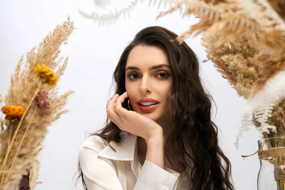 Femme souriante encadrée par des plantes sèches.